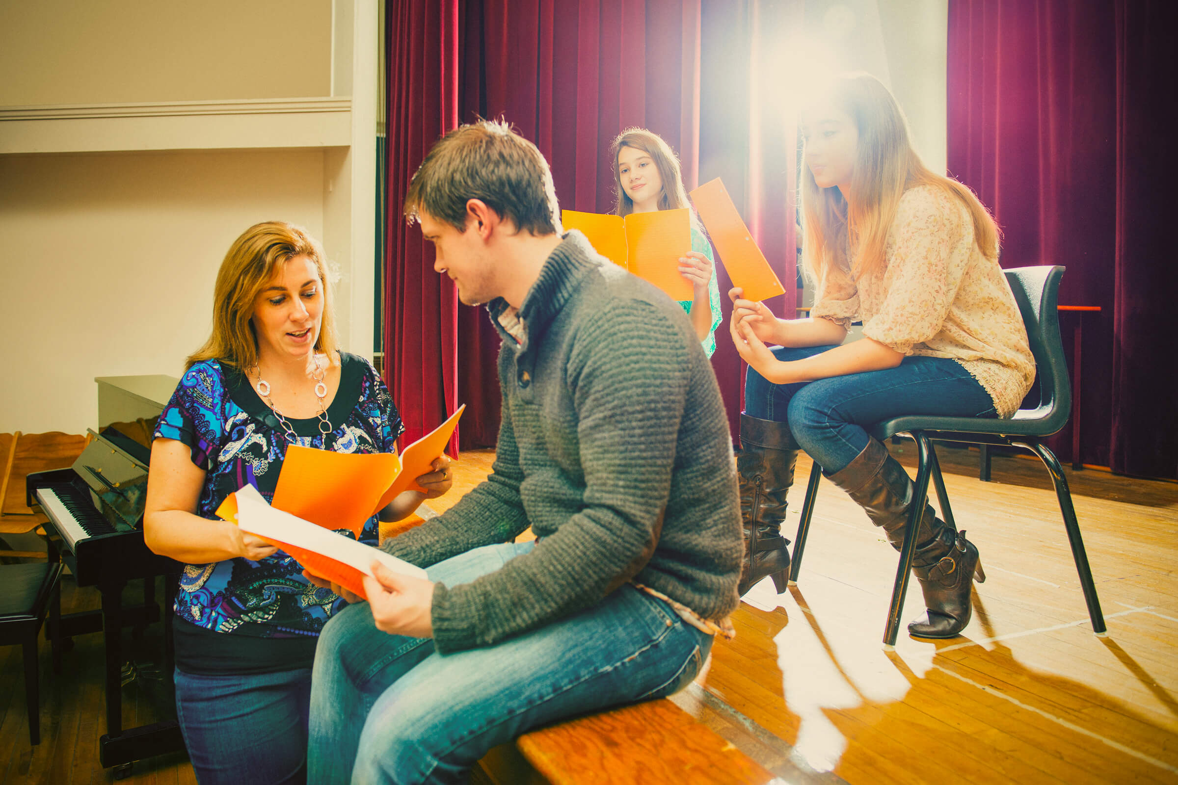 A drama teacher reviewing scripts with students on a school stage