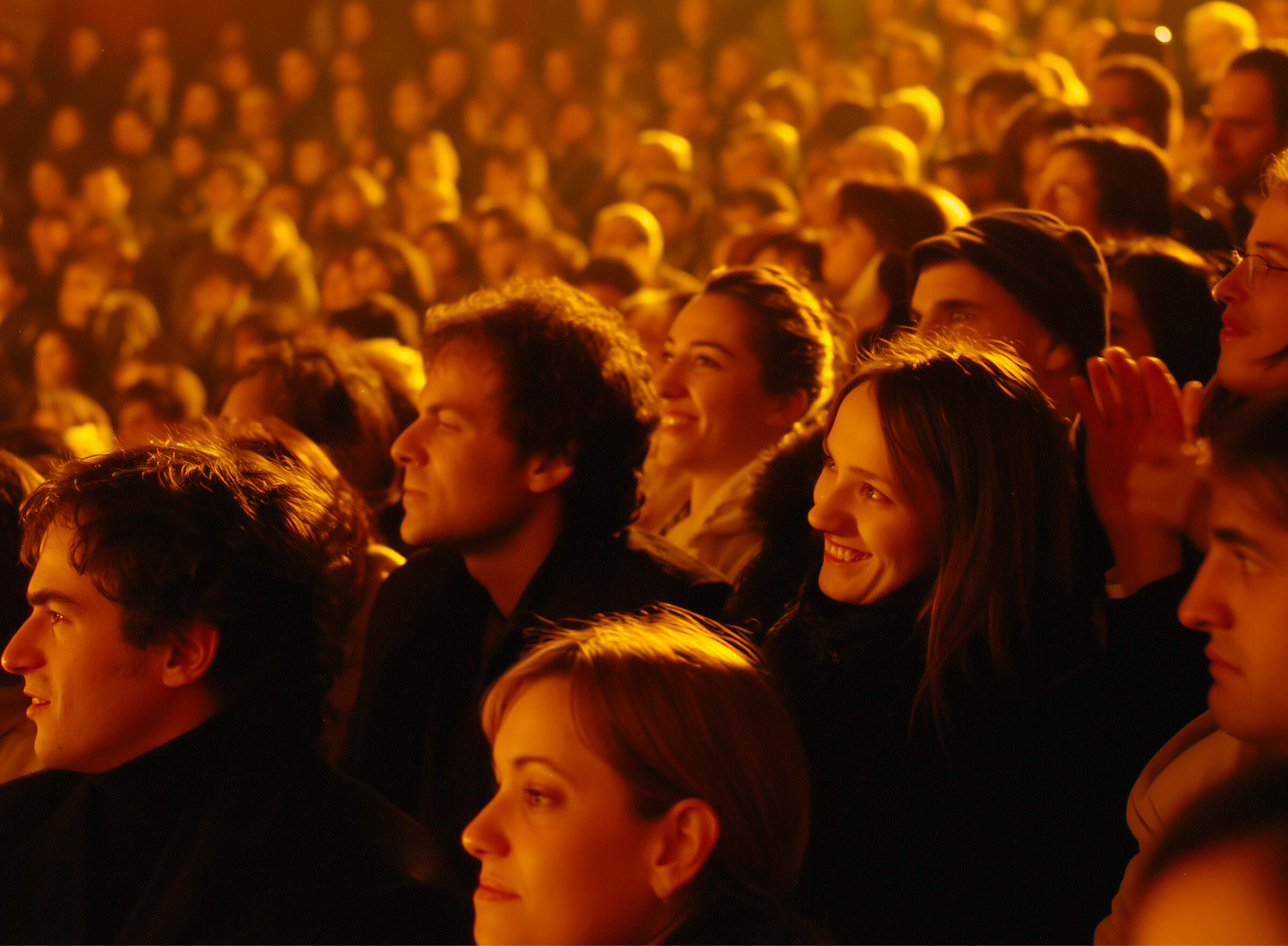 A smiling, engaged audience watching a show in warm theater light