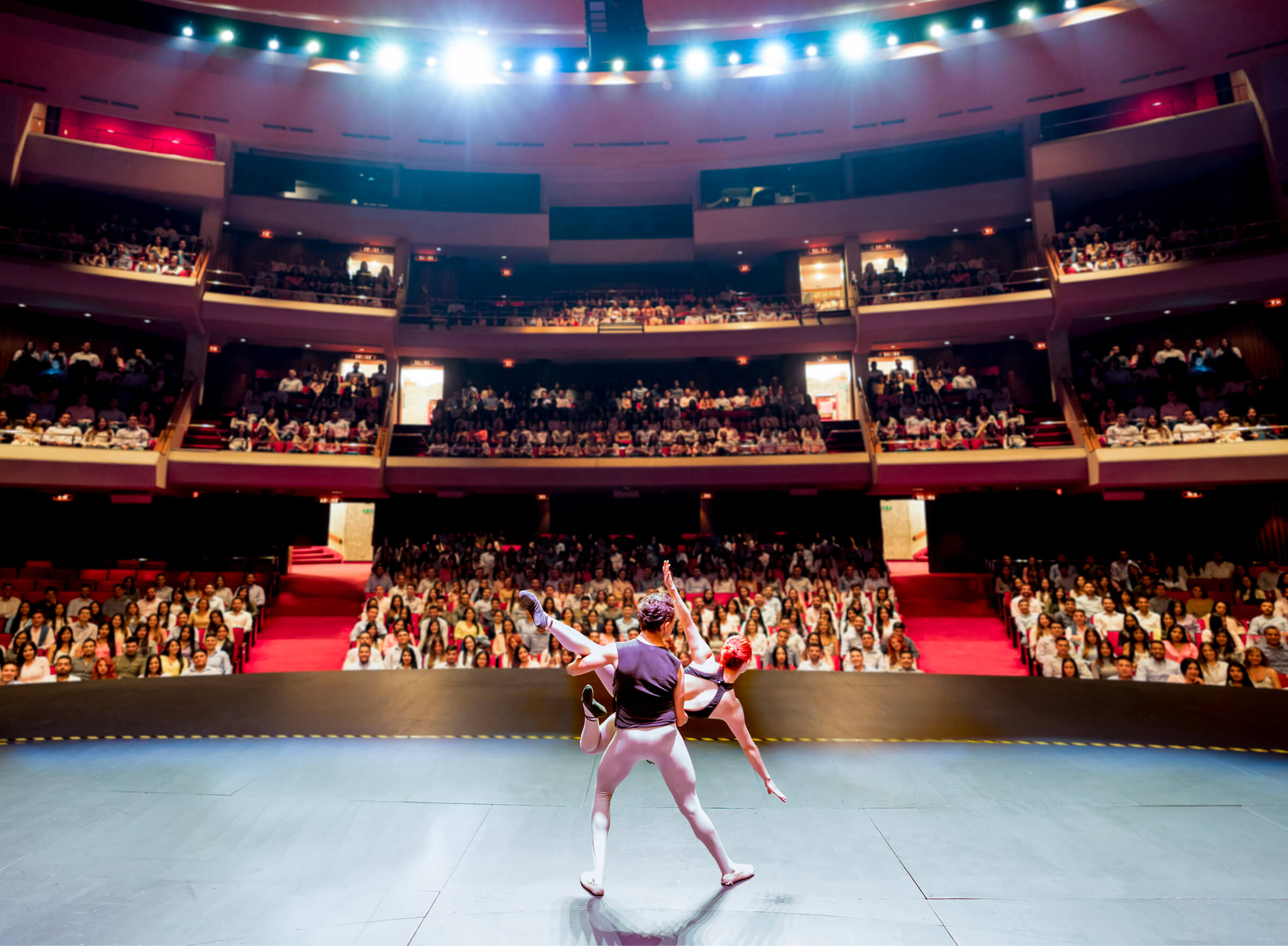 A full house in a grand multi-tier performing arts center, seen from the stage