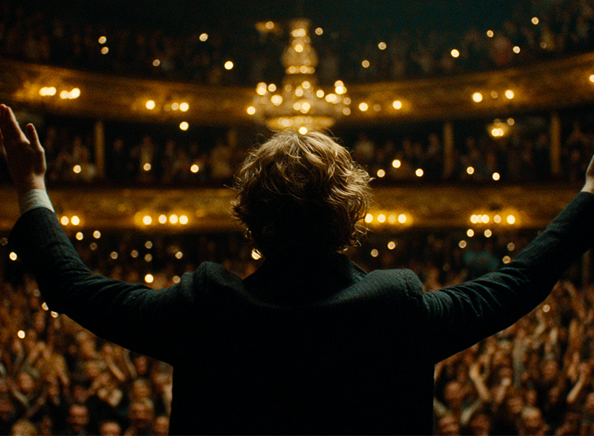 A performer with arms raised to a packed opera house